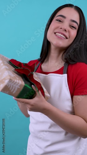 Young latina female shop assistant smiling while offering a wrapped gift for the holidays