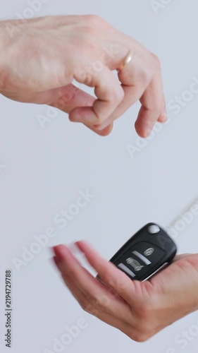 Vertical video. Man hand gives a car keys to woman hand in the car dealership close up. Unrecognized auto seller.