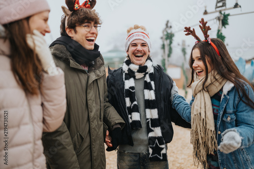 Фотография A group of young friends laugh together outdoors wearing winter coats and Christmas headbands
