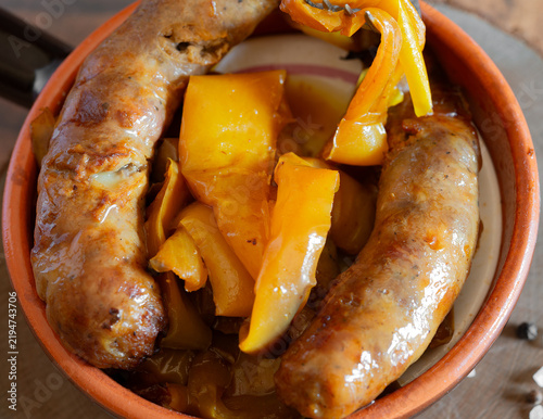 Sausages with yellow peppers in terracotta bowl