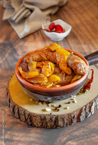 Sausages with yellow peppers in terracotta bowl