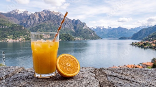 Fresh orange juice with ice in a glass against the background of a beautiful mountain lake