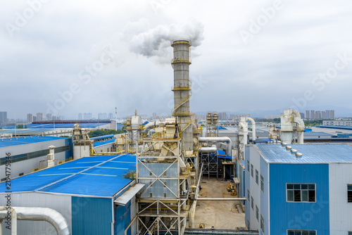 Bild auf Leinwand Blue factory building chimney emitting white smoke into the sky