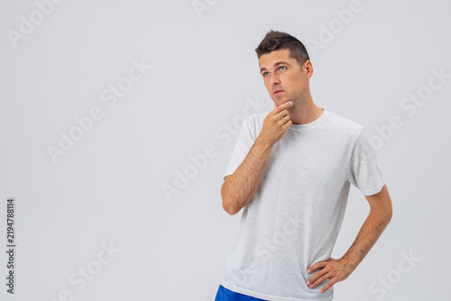 Obraz na płótnie Thoughtful young Caucasian man touching his chin in deep thought against a plain studio background