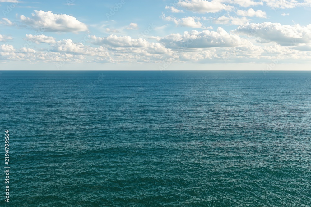 Fototapeta premium Vast blue ocean horizon under a bright sky with scattered white clouds on a sunny summer day