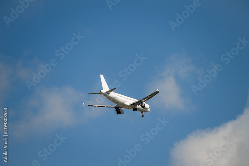 Obraz na plátně A white passenger airplane descends through a blue sky with soft white clouds, preparing for landing with its gear extended