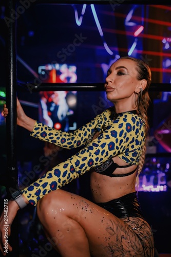 Go-go dancer in leopard print stagewear poses beside a nightclub railing under vivid blue neon lights, creating a bold nightlife image for dance, entertainment and event advertising