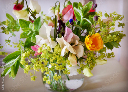 A colorful summer bouquet of sweet peas, marigold, and garden foliage sits in a glass jar.
