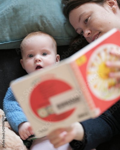 Mother and baby girl lying down with picture book
