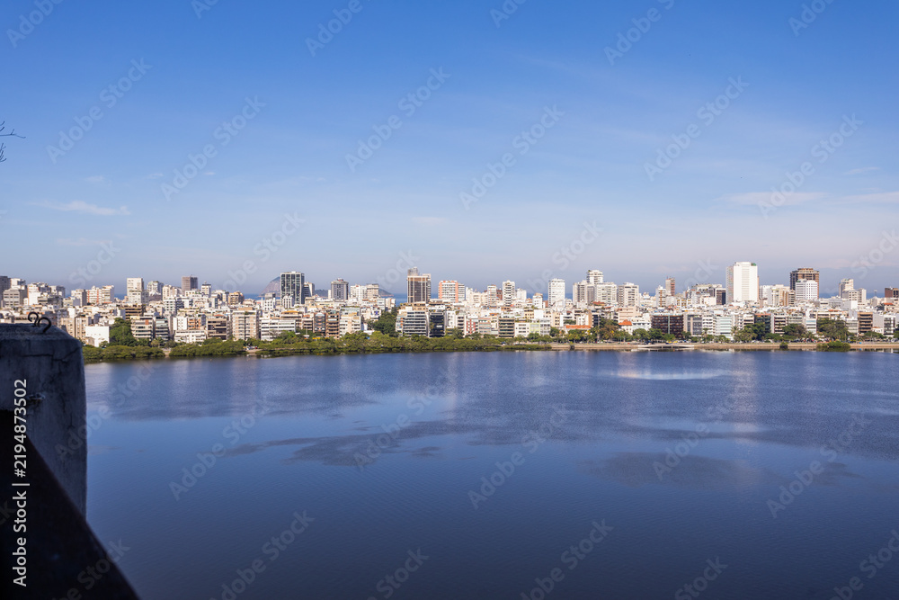 Obraz premium Panoramic view of the Rio de Janeiro skyline across the calm waters of Lagoa Rodrigo de Freitas under a clear blue sky in Brazil