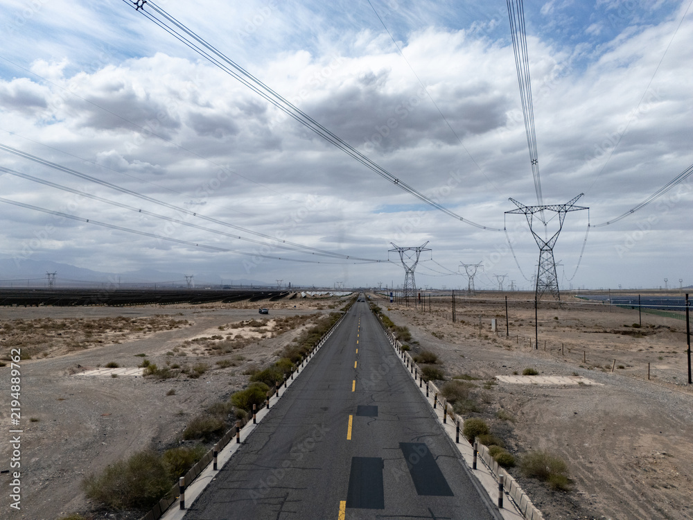 Fototapeta premium Desert highway stretching towards distant power transmission towers under cloudy sky
