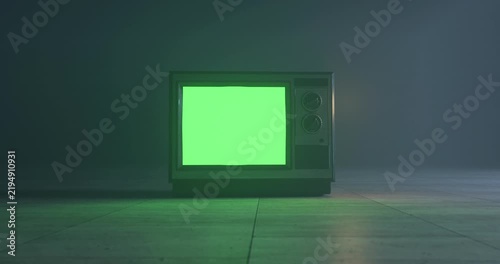 Vintage television turning on with green screen display and rotating knobs in dark foggy room