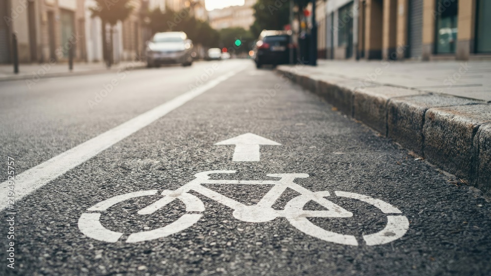 Obraz premium White bicycle lane symbol painted on asphalt street with blurred cars