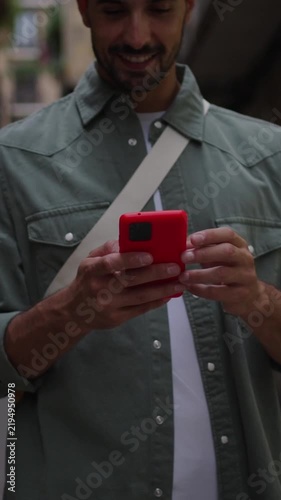 Close-up of a man using cellphone while walks in a street of an old town, sending online messages and using social media apps. Vertical video.