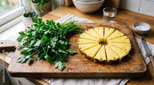 Wooden cutting board with fresh parsley on left and triangular pineapple slices arranged in circular pattern on right, vibrant color contrast.