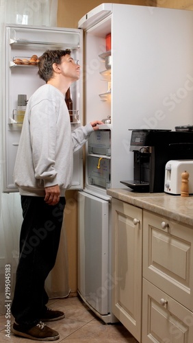 Obraz na plátně Hungry man searching for food in an open household refrigerator in the kitchen,