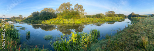 Beautiful morning landscape with a shallow river, in which trees and the sky are reflected in the rays of the morning sun. Dawn in nature in summer. Ukraine, Europe.