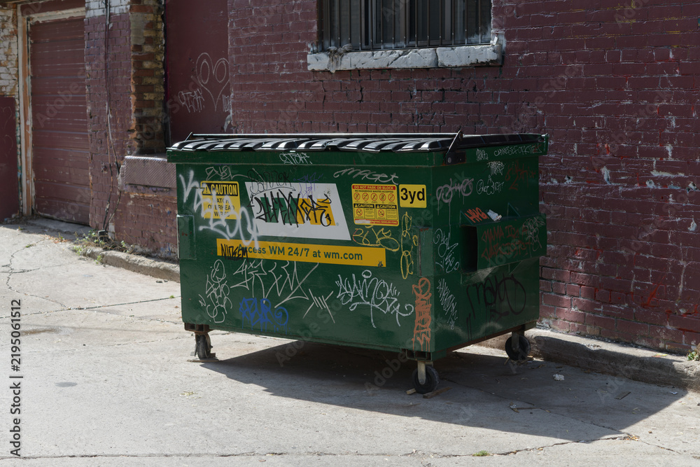 Fototapeta premium WM commercial wheeled waste container with a split (two-flap) lid in a lane in Toronto