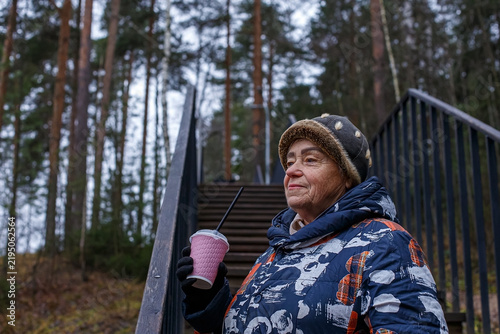 A cute elderly woman is walking in a nature park and enjoying a quiet autumn day.