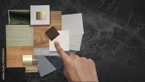 Interior Designer Hand Pointing at Material Swatch Sample Board: Wood Veneer, Tile, Fabric, Velvet, and Metal Finishes Arranged on Dark Marble Countertop for Architect Selection and Home Renovation.