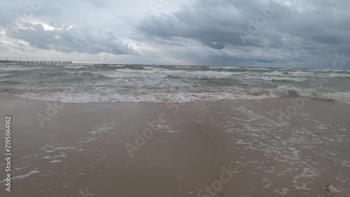 Rough sea waves washing onto sand beneath storm clouds