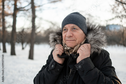 Mature Caucasian man adjusting the collar of his warm coat outdoors in a snowy park, protecting himself from cold winter weather.