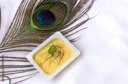 Peacock feather symbolic to Hindu god Lord Krishna or laddu Gopal with butter candy and saffron during celebration of Janmashtami festival concept, isolated on white background.