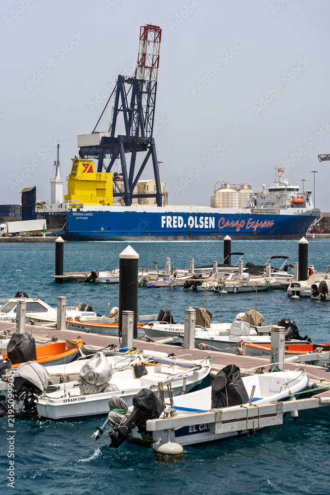 Fototapeta premium PUERTO DEL ROSARIO, FUERTEVENTURA – AUGUST 1, 2026: Cargo vessel and small boats moored in harbor with port cranes in the capital of Fuerteventura.