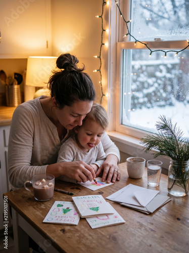 Mother helping her young child write holiday cards at a cozy winter table, capturing authentic family milestones and seasonal traditions.