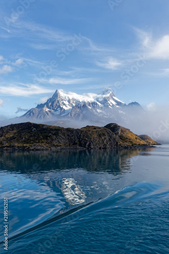 Snow covered peaks of Torres del Paine rising above morning fog and turquoise glacial waters of Lake Pehoe in Chilean Patagonia.