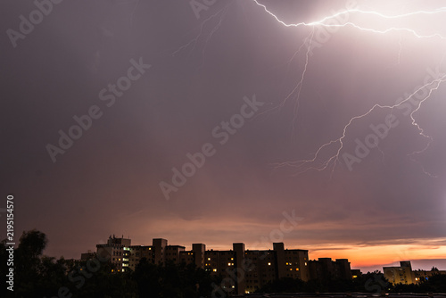 Powerful Lightning Illuminates Storm Clouds Above City at Dusk