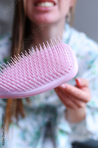 Close-up of woman showing loose hair caught in a brush, illustrating hair loss, shedding and concern about scalp health.