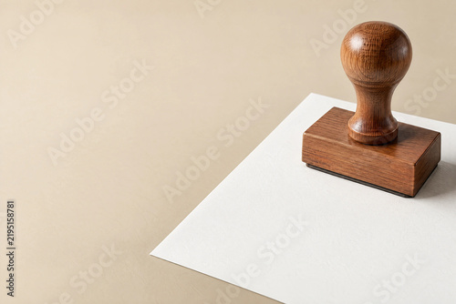 Wooden stamp pressing onto a blank document sheet on sand beige