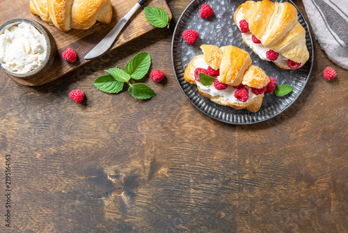 Sweet breakfast croissant sandwich with raspberries and cream cheese. Homemade and healthy french croissant for breakfast. Top view flat lay background. Copy space.