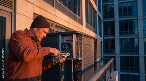 Emergency technician repairs condenser on office facade