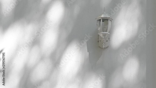 Vintage Wall Lantern with Moving Tree Shadows on White Stucco Wall, Sunlight and Architectural Background.