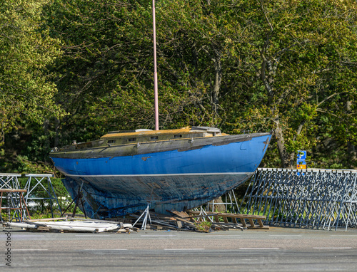 Quadro su tela Weathered blue sailboat stored ashore among marina stands.