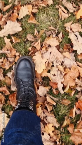 Legs walking on autumn dry leaves. Top view of female legs walking in autumn park. Vertical video. First person view of legs in boots walking on fallen maple and oak leaves. Autumn walk