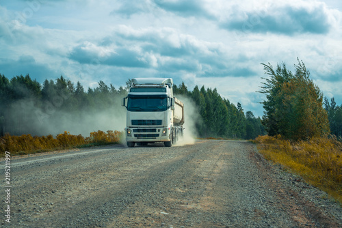 Heavy dump truck driving on a dusty gravel road through countryside
