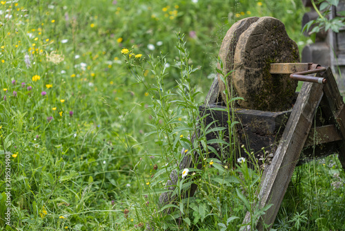 Obraz na płótnie A rustic manual stone mill on a weathered wooden stand, positioned in a lush summer meadow