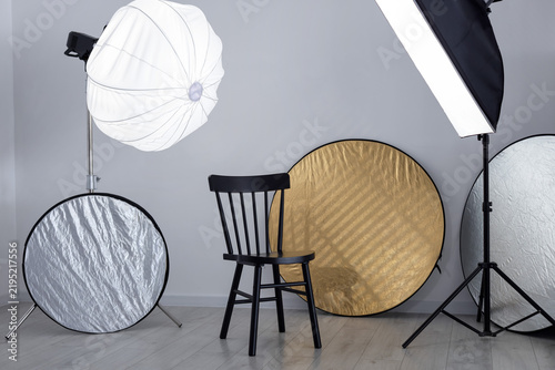 Different modern lighting equipment and chair in photo studio