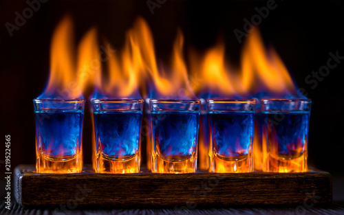 The Flaming Shot Glasses With Blue Liquid Under Dark Dramatic Lighting