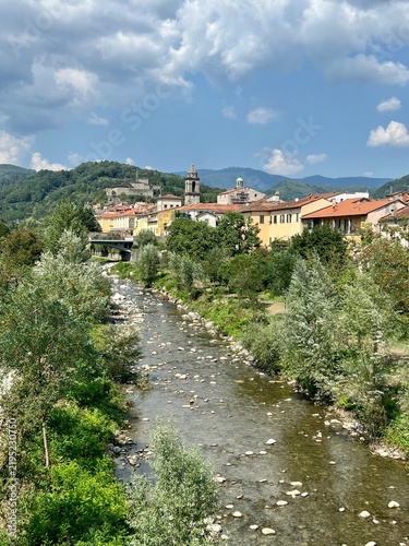Scenic view of Pontremoli in Lunigiana, Tuscany, Italy, with the town surrounded by green hills and mountains. The river flows through the foreground toward the historic centre,.