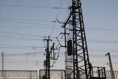 Vue en perspective d'un pylône électrique en ossature métallique, portant des lignes à haute tension. Structure dédiée au transport de l'énergie par voie aérienne. Ciel bleu en arrière plan.