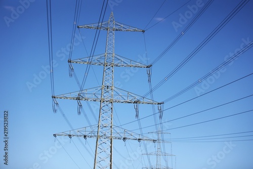 Vue en perspective d'un pylône électrique en ossature métallique, portant des lignes à haute tension. Structure dédiée au transport de l'énergie par voie aérienne. Ciel bleu en arrière plan.