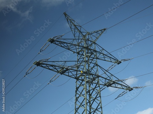 Vue en perspective d'un pylône électrique en ossature métallique, portant des lignes à haute tension. Structure dédiée au transport de l'énergie par voie aérienne. Ciel bleu en arrière plan.