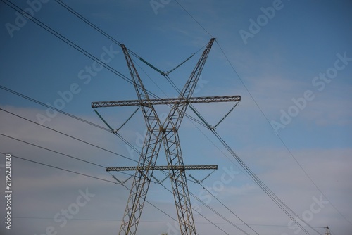 Vue en perspective d'un pylône électrique en ossature métallique, portant des lignes à haute tension. Structure dédiée au transport de l'énergie par voie aérienne. Ciel bleu en arrière plan.