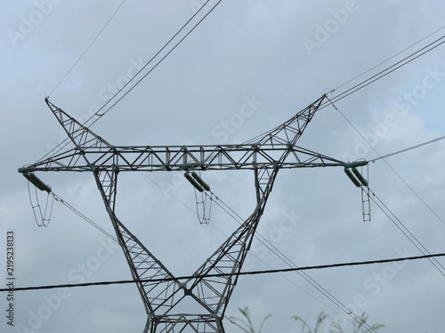 Vue en perspective d'un pylône électrique en ossature métallique, portant des lignes à haute tension. Structure dédiée au transport de l'énergie par voie aérienne. Ciel bleu en arrière plan.