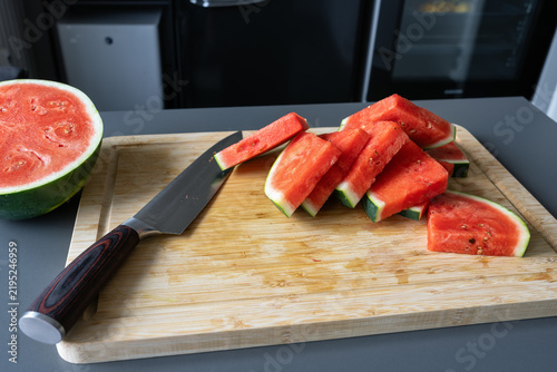 Sliced watermelon pieces with kitchen knife on wooden cutting board in modern kitchen