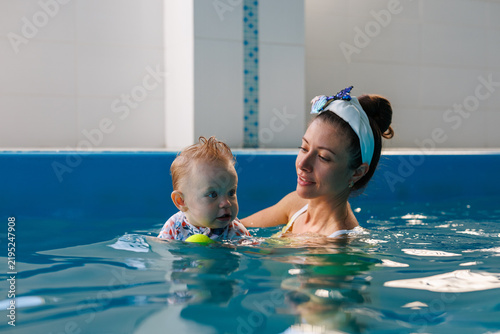 A mother holds a baby above the water surface in an indoor pool